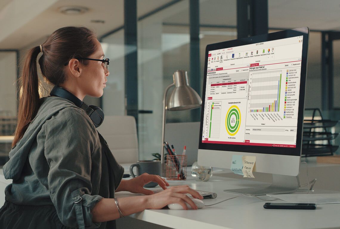 A woman sits in front of a monitor and processes the evaluation of a manufacturing-related inspection
